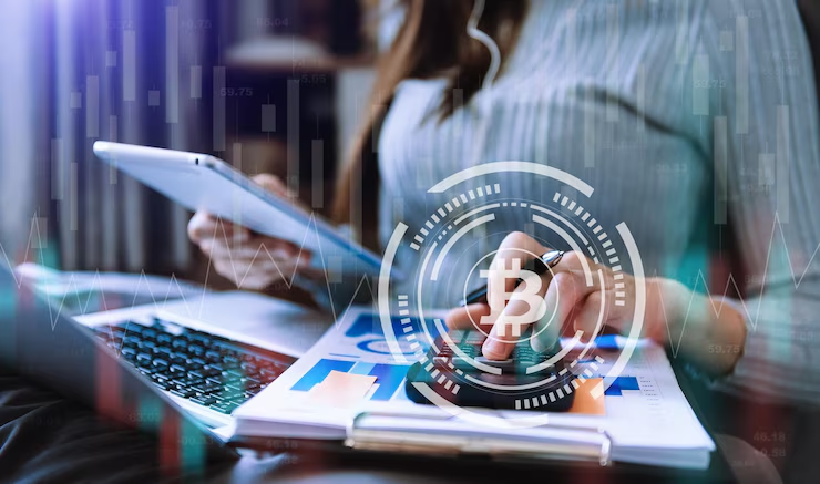 Person working on laptop and tablet with a calculator, overlaid with Bitcoin icon and financial charts, representing cryptocurrency business or analysis.