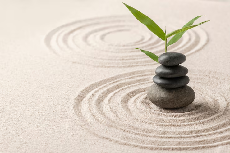 A stack of smooth stones with a bamboo sprout in a raked sand Zen garden, symbolizing tranquility and balance.